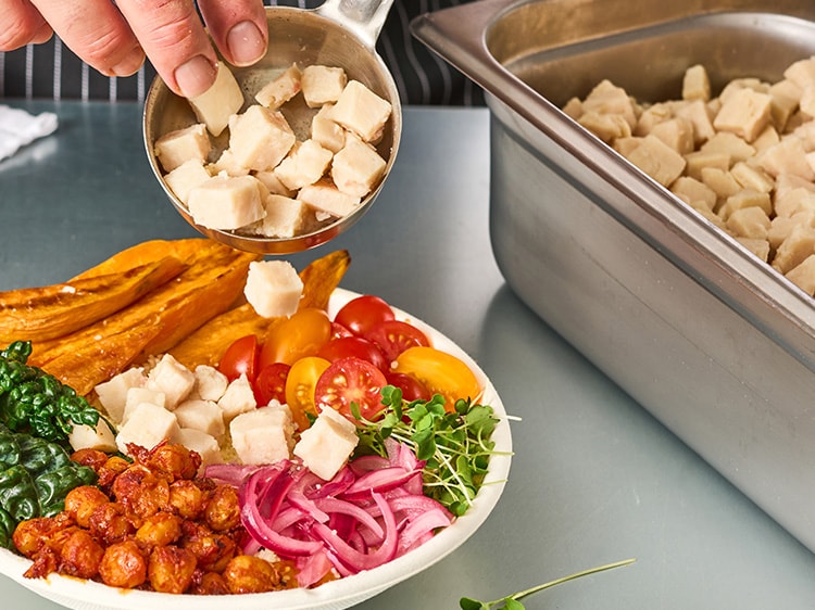 Person scooping diced meat into a bowl of veggies.